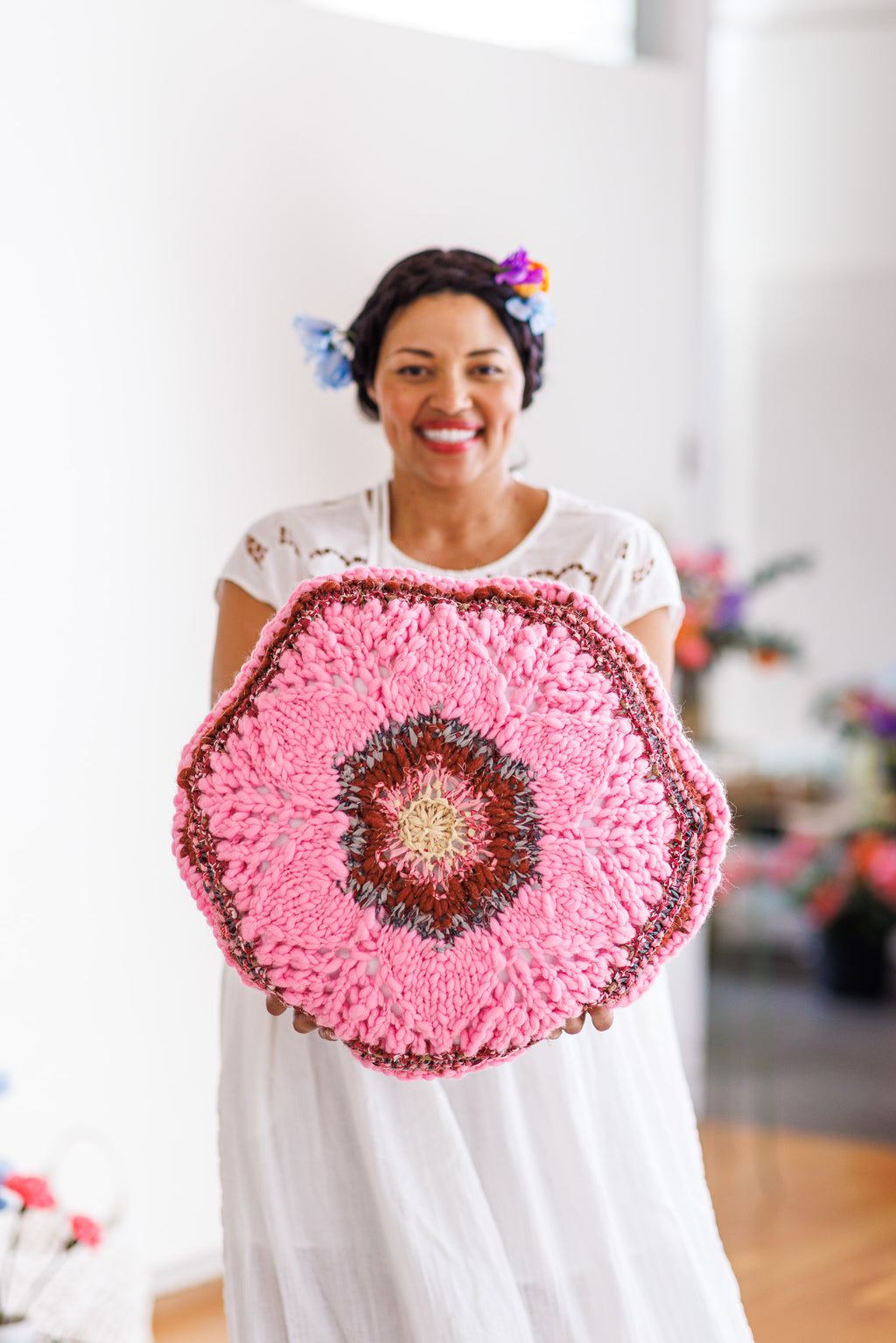 Smiling model holding pink pillow with centered floral motif in front of body