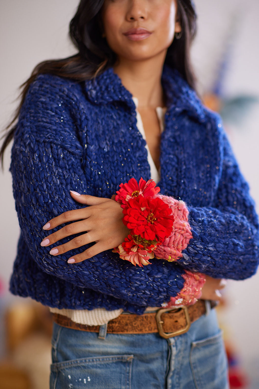 Models arms are crossed in front of body displaying sleeves  of wool cardigan with cuff ribbing detail and flower bracelet