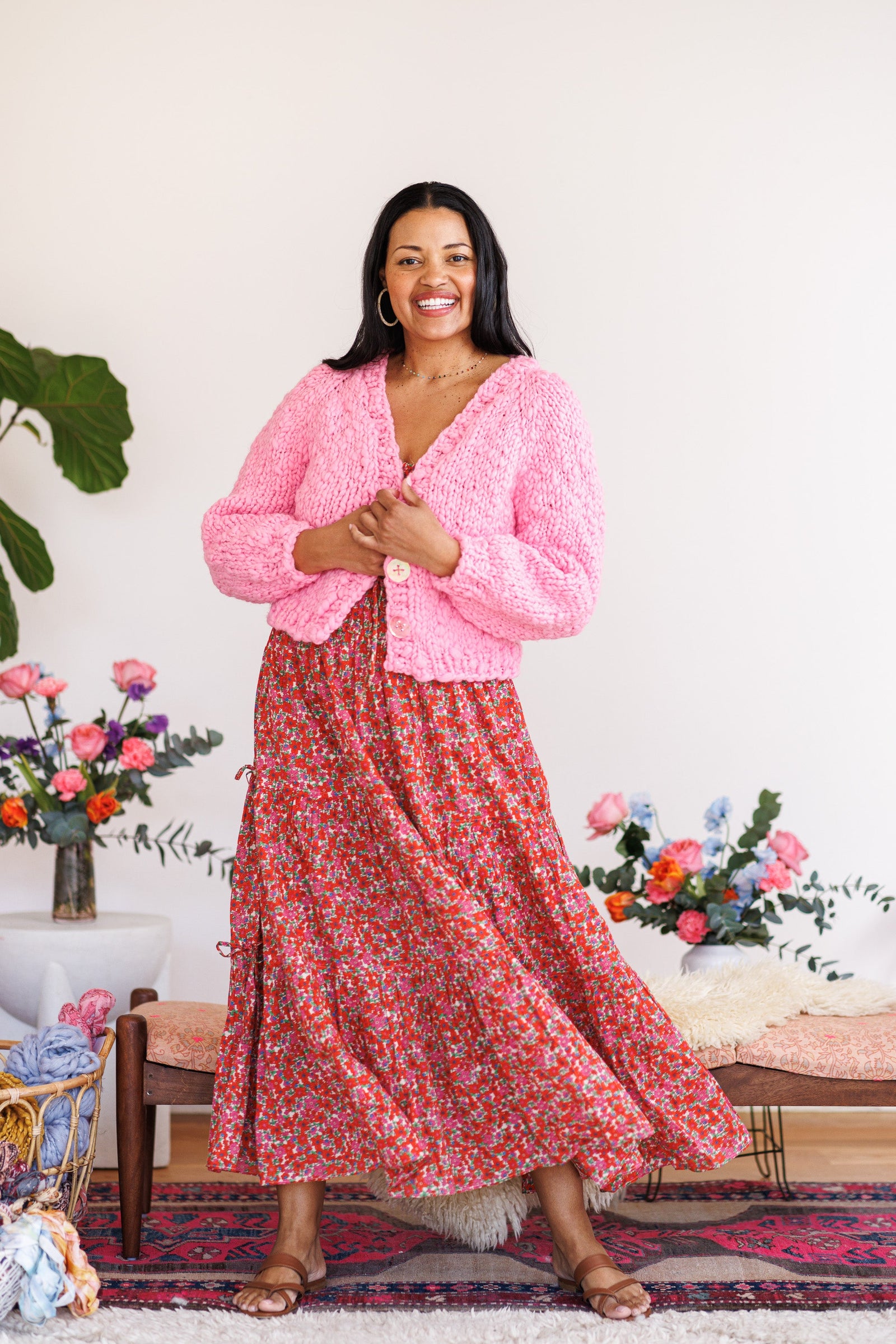 Smiling model holding pink wool cardi closed over red floral dress