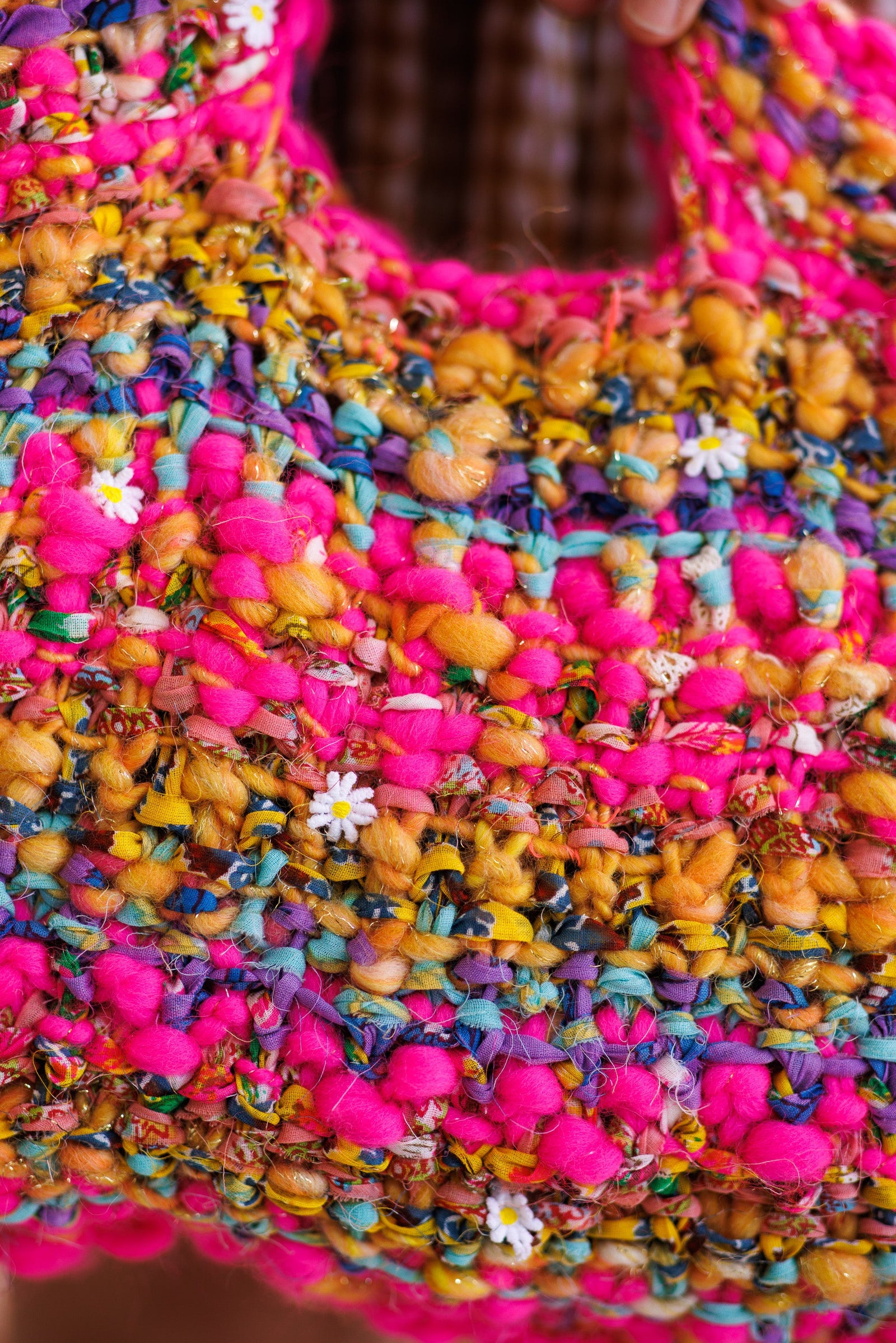 Close-up of stitch pattern on striped, wool and cotton yarn handbag highlighting small fabric daisies within the yarn