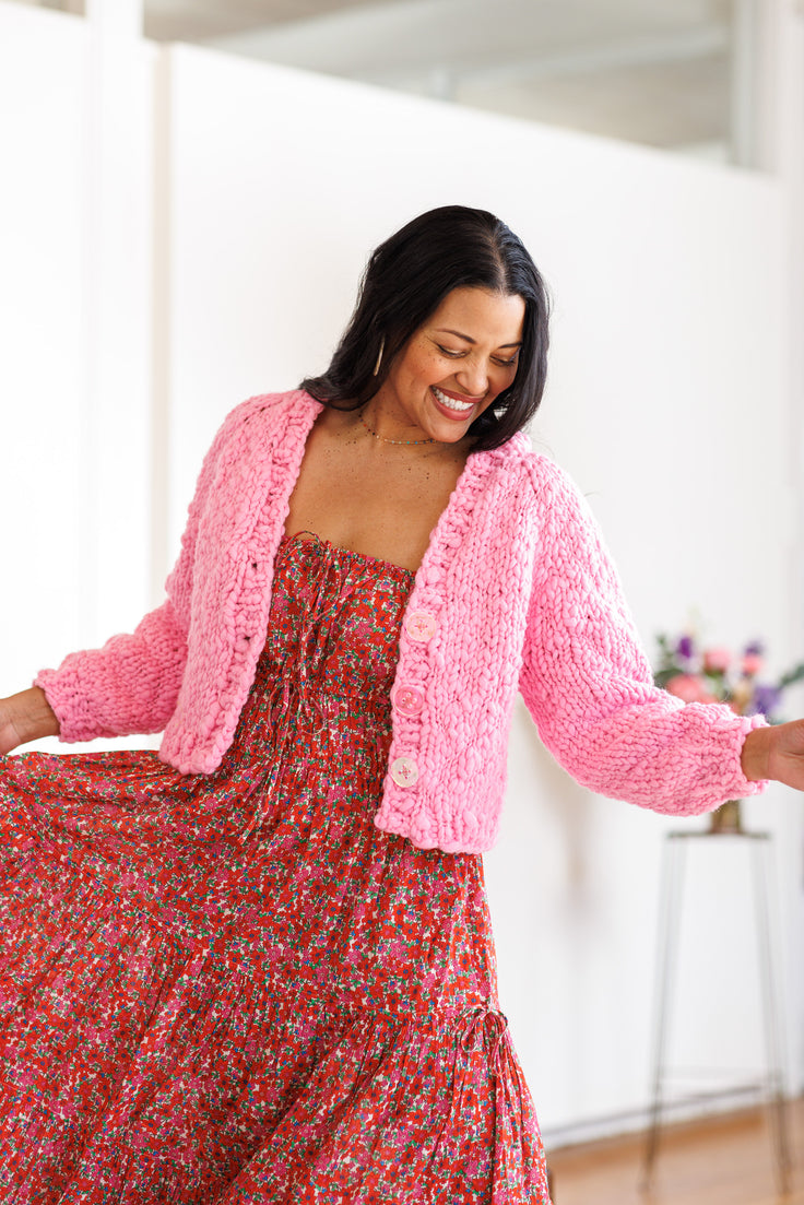 Model is smiling and twirling wearing red dress with pink cardi over the top.