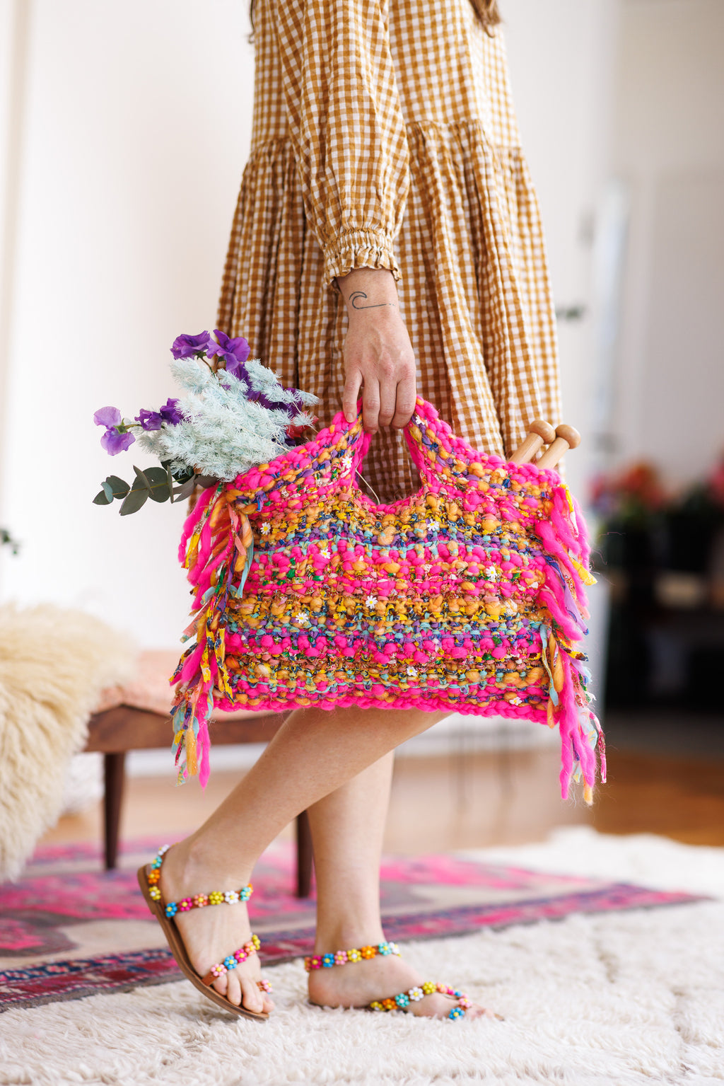 Model holding the handles of a wool and cotton knit, striped handbag containing flowers and knitting needles