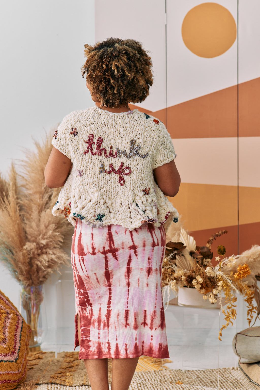 Model turned away from the camera to reveal a cardigan that says Think Up on the back