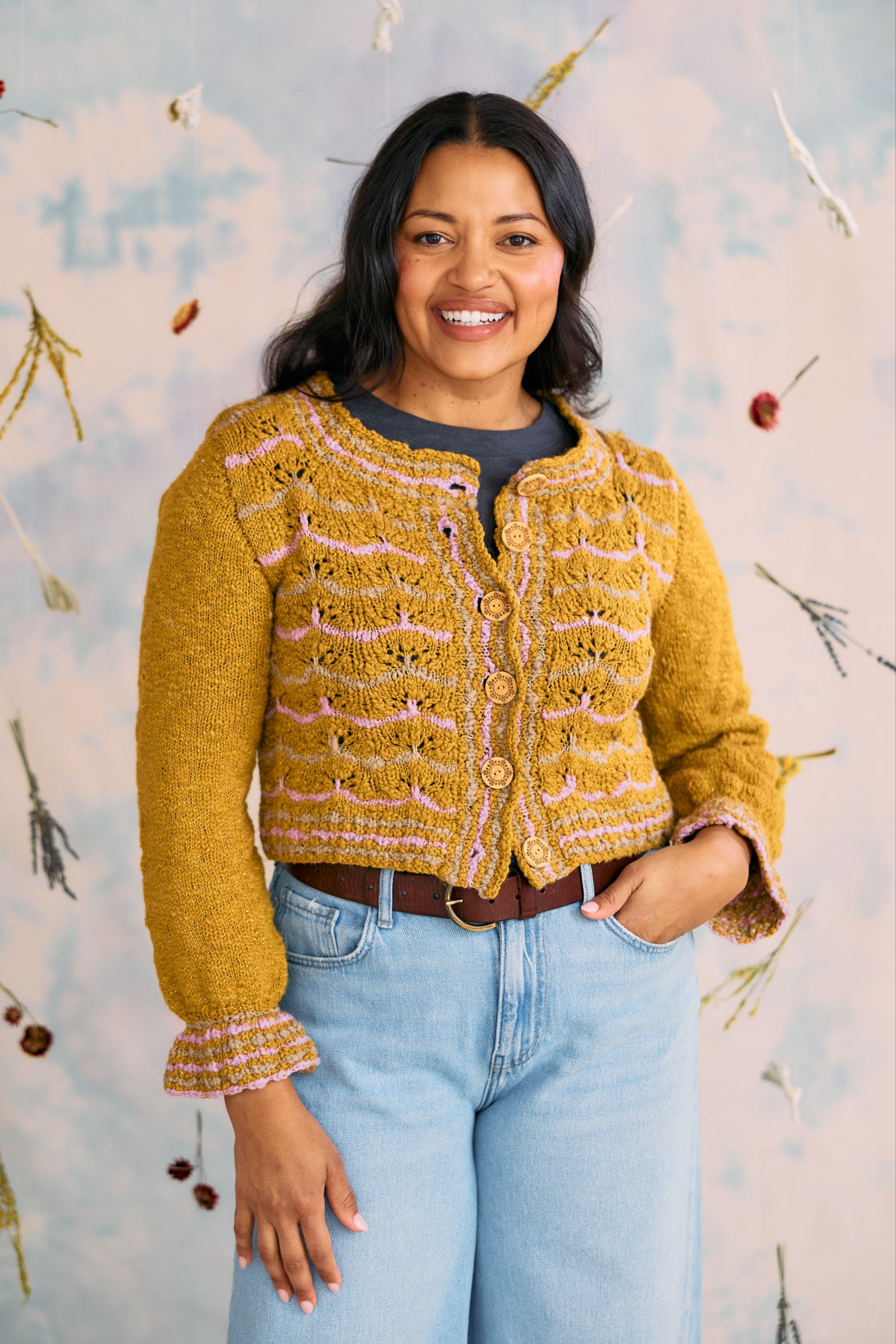 Woman wearing a yellow knit cardigan against a decorative wall.