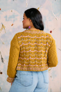 Person wearing a yellow textured handknit sweater against a floral background