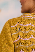 Close-up of a mustard yellow knitted lace sweater with pink and beige patterns.