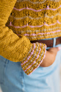Close-up of a mustard yellow sweater with pink and tan striped ruffled cuffs and hem.
