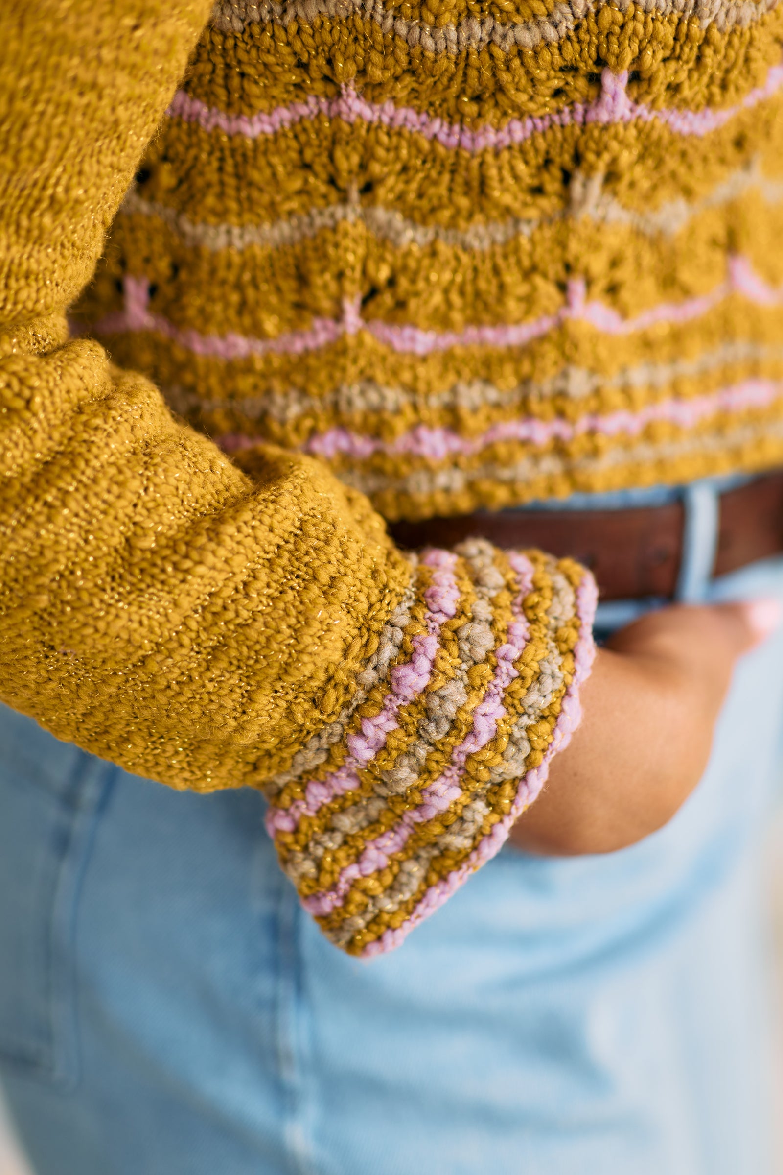 Close-up of a mustard yellow sweater with pink and tan striped ruffled cuffs and hem.