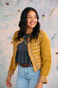 Woman wearing a mustard yellow knitted cardigan with a floral pattern against a light blue background.