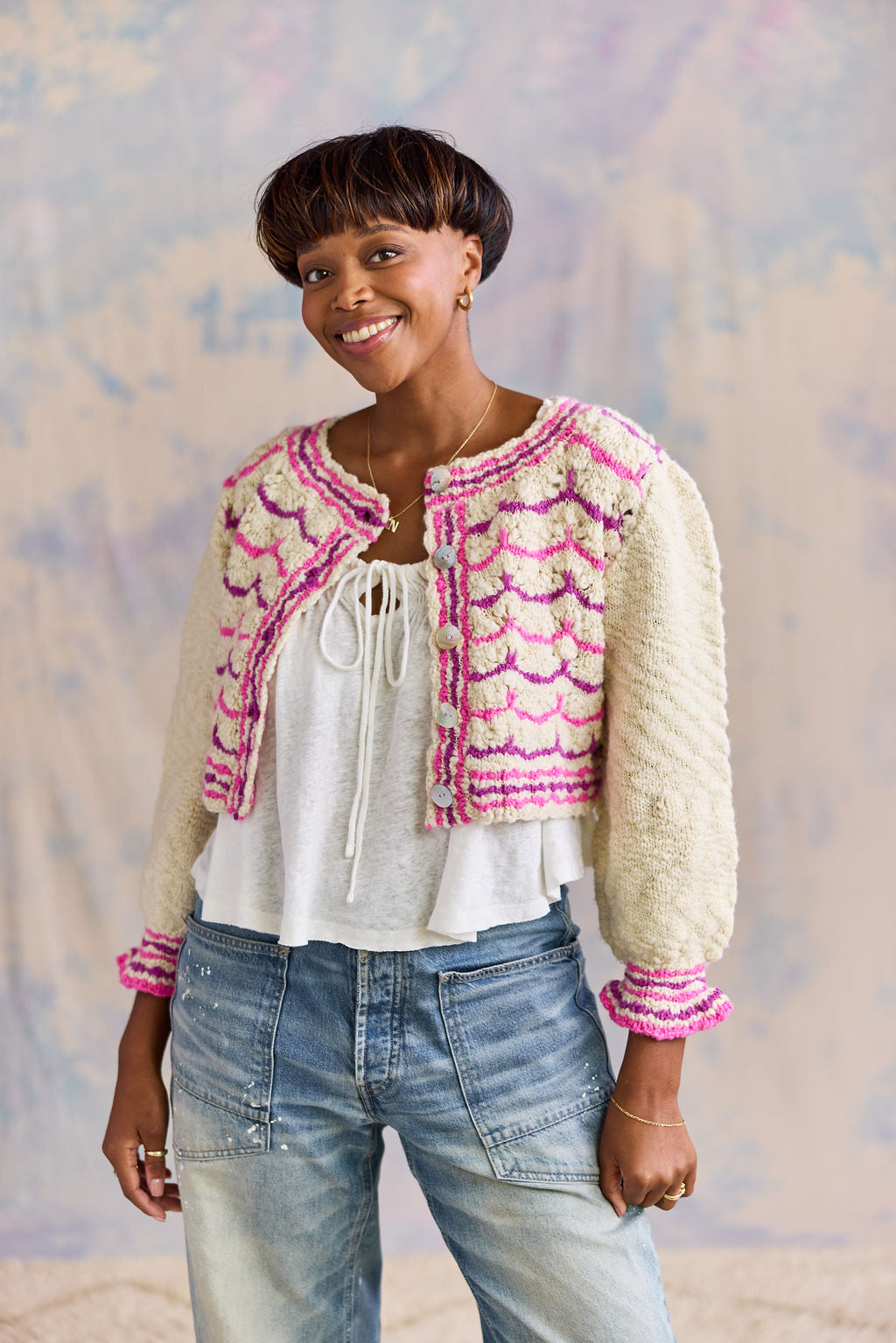 Woman wearing a colorful knitted cardigan against a textured wall.