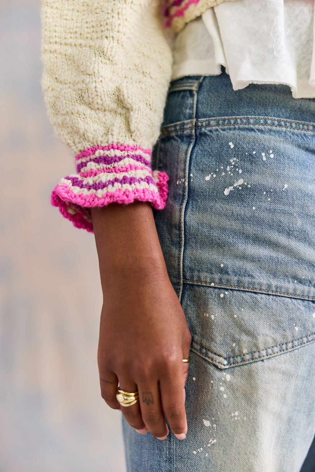 Person wearing a textured sweater with colorful ruffle cuffs and blue jeans.