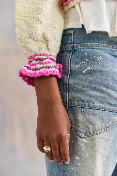 Person wearing a textured sweater with colorful ruffle cuffs and blue jeans.