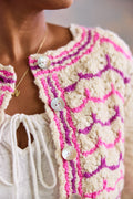 Close-up of a person wearing a pink and white lace patterned cardigan with pearl buttons.