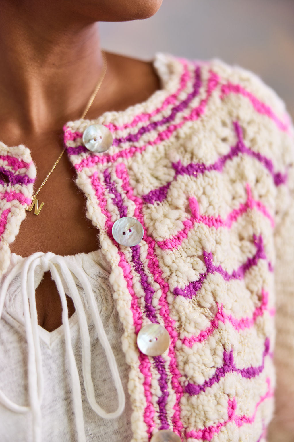 Close-up of a person wearing a pink and white lace patterned cardigan with pearl buttons.