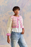Woman wearing a pink and white patterned cardigan with a white top and blue jeans against a neutral background