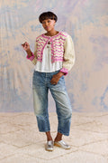 Woman wearing a patterned cardigan, white shirt, blue jeans, and silver shoes against a textured wall.