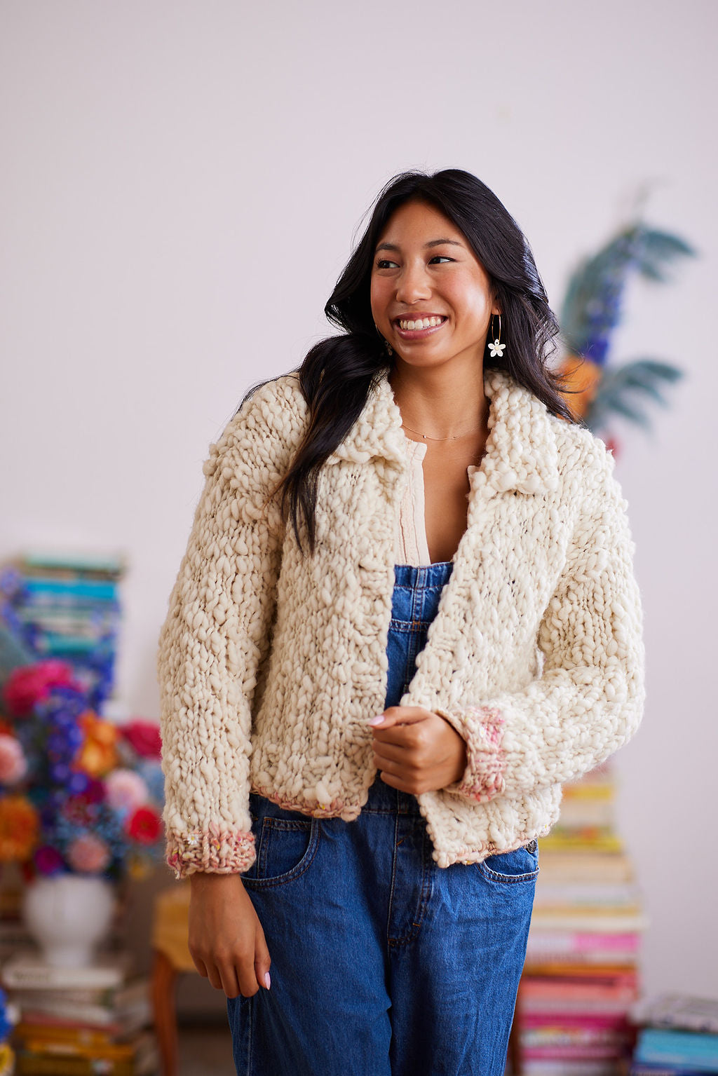 Smiling model wearing cream wool cardigan with color over denim overalls