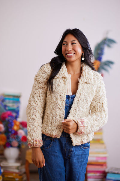 Smiling model wearing cream wool cardigan with color over denim overalls