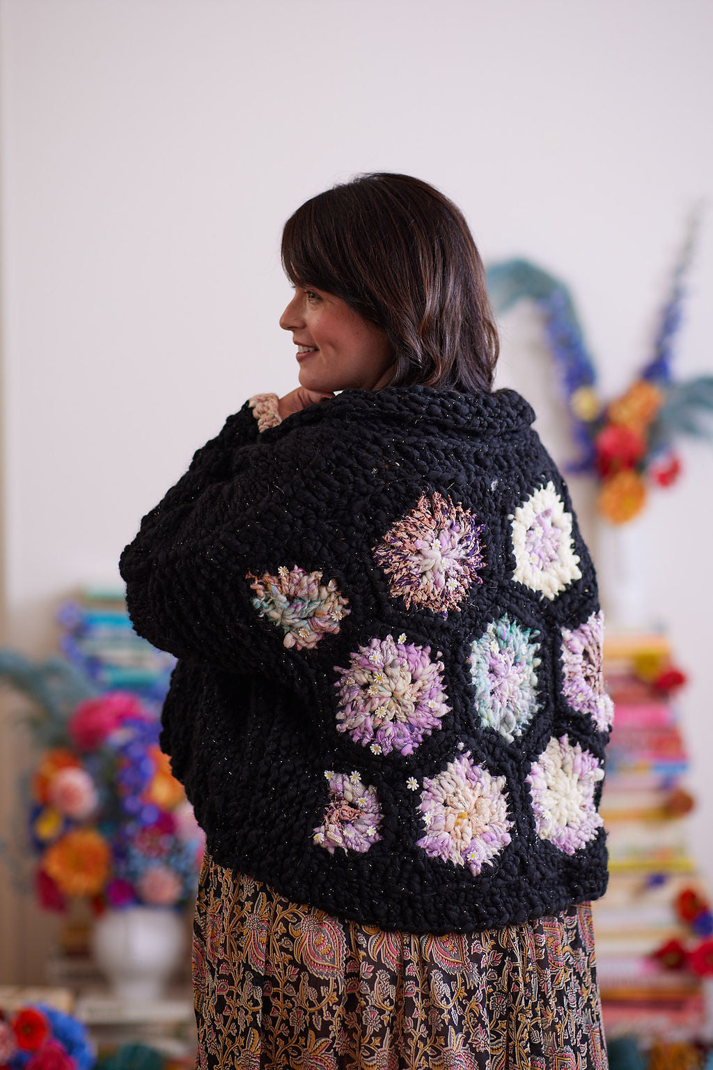 Smiling model displaying back of black knit and crochet cardigan featuring pastel crochet hexagons