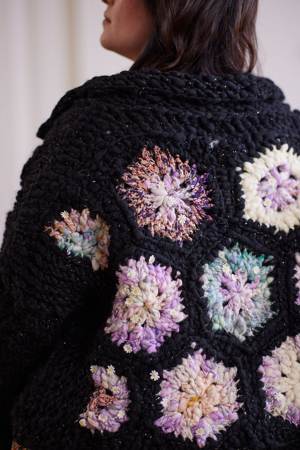Close up of black knit and crochet cardigan with metallic sparkles  featuring pastel crochet hexagons with little daisies in yarn