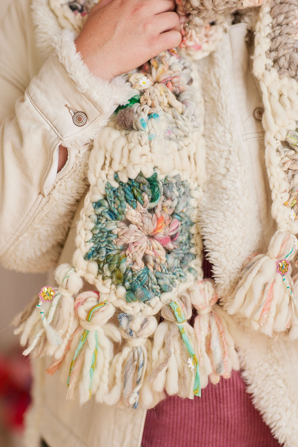 Close up view of crochet hexagon detail in multicolored yarn, also displaying tassel detail at end of scarf 