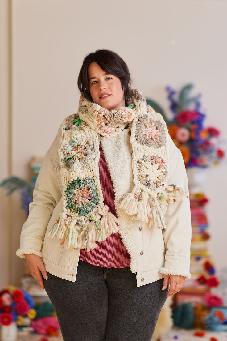 Model wearing crochet scarf wrapped around neck displaying tassels on each end of scarf