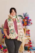 Model smiling while holding the at tassels each end of the crochet scarf