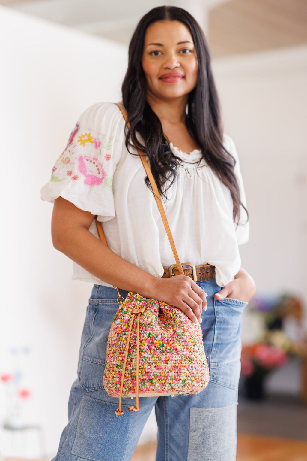 Model wearing a multicolored, cotton crochet bucket bag with shoulder strap