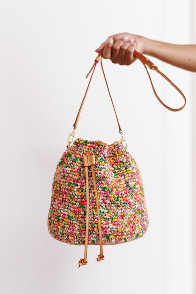 Model using one hand to hold bag out in front of blank, white wall