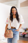 Smiling model wearing bucket bag on shoulder, resting hand toward bottom base of bag with other hand in pocket of denim jeans