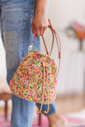 Model holding multicolored, cotton, crochet bucket bag with one hand on the brown leather strap