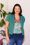 Model wearing unbuttoned, short-sleeve green cardi over multicolored top and denim jeans