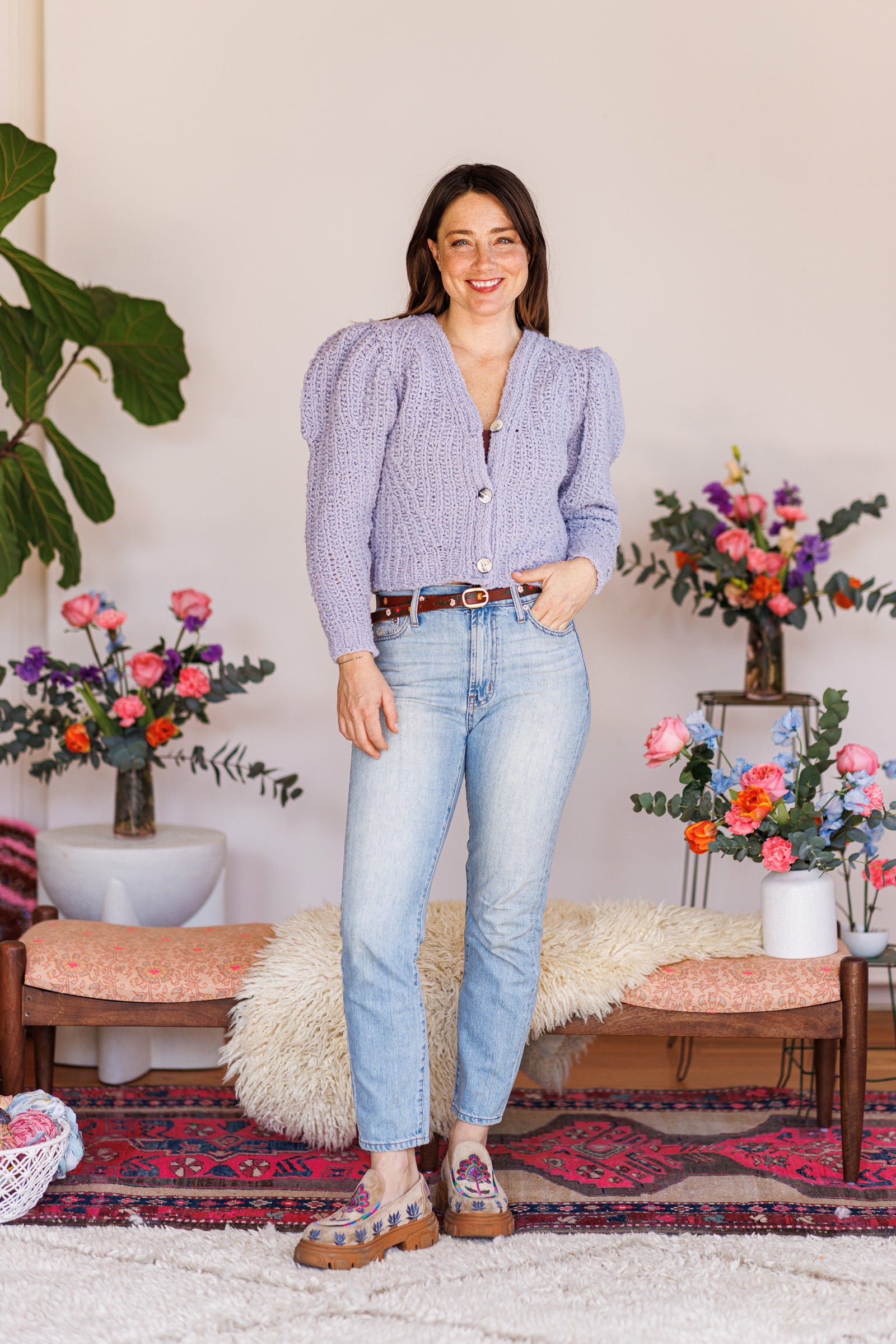 Smiling model wearing long-sleeve knit cardigan with one hand in pocket of denim jeans