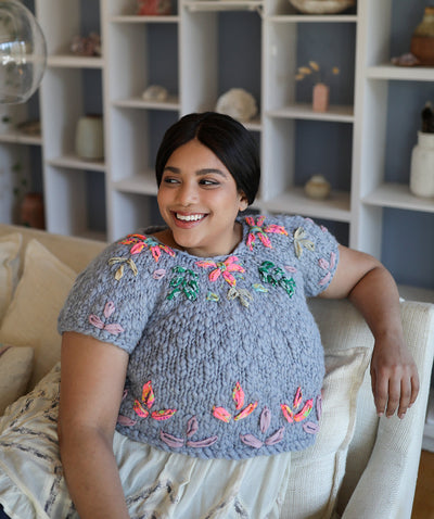 Model sitting down looking to side while wearing the second version of the sweater