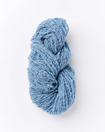 A skein of brushed boucle yarn in a dusty denim blue color