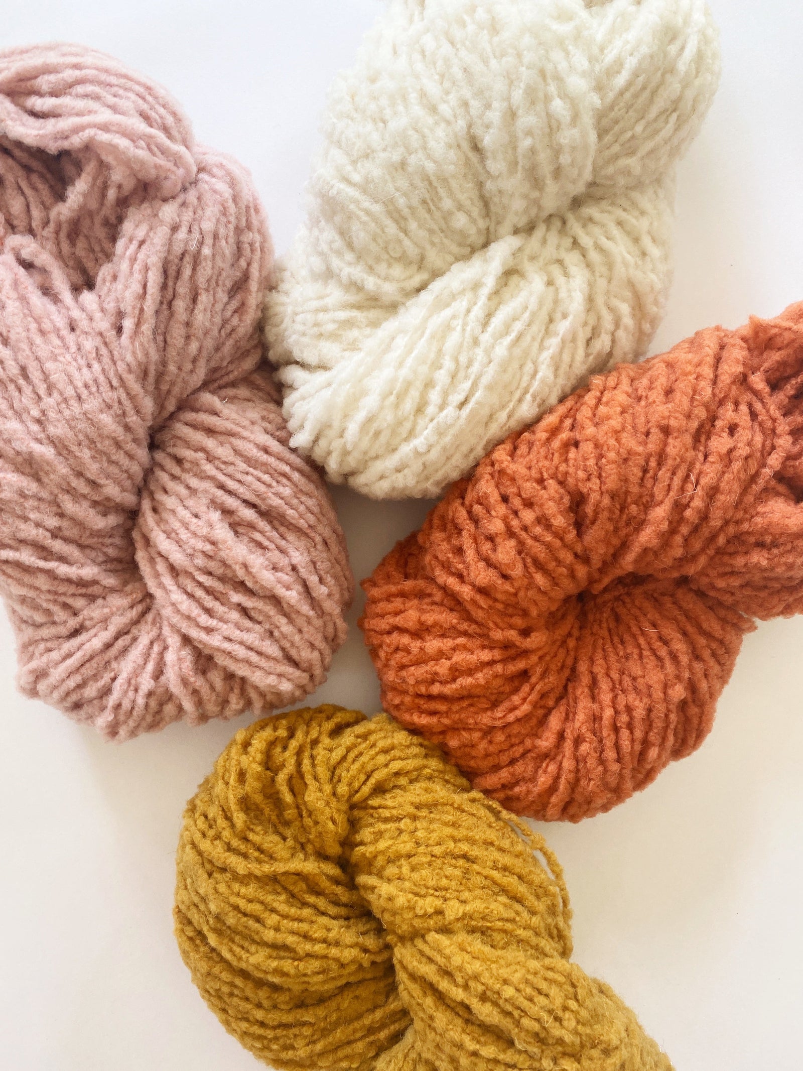 A brushed boucle yarn shown in 4 colors: tan, white, burnt orange, and marigold yellow