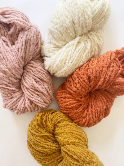 4 skeins of brushed boucle yarn shown together in the colors tan, ivory, burnt orange, and marigold yellow.