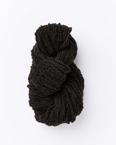 A skein of brushed boucle yarn in a dark charcoal grey almost true black color.