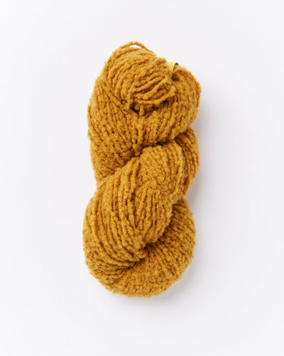 A skein of brushed boucle yarn in a marigold ochre mustard yellow color