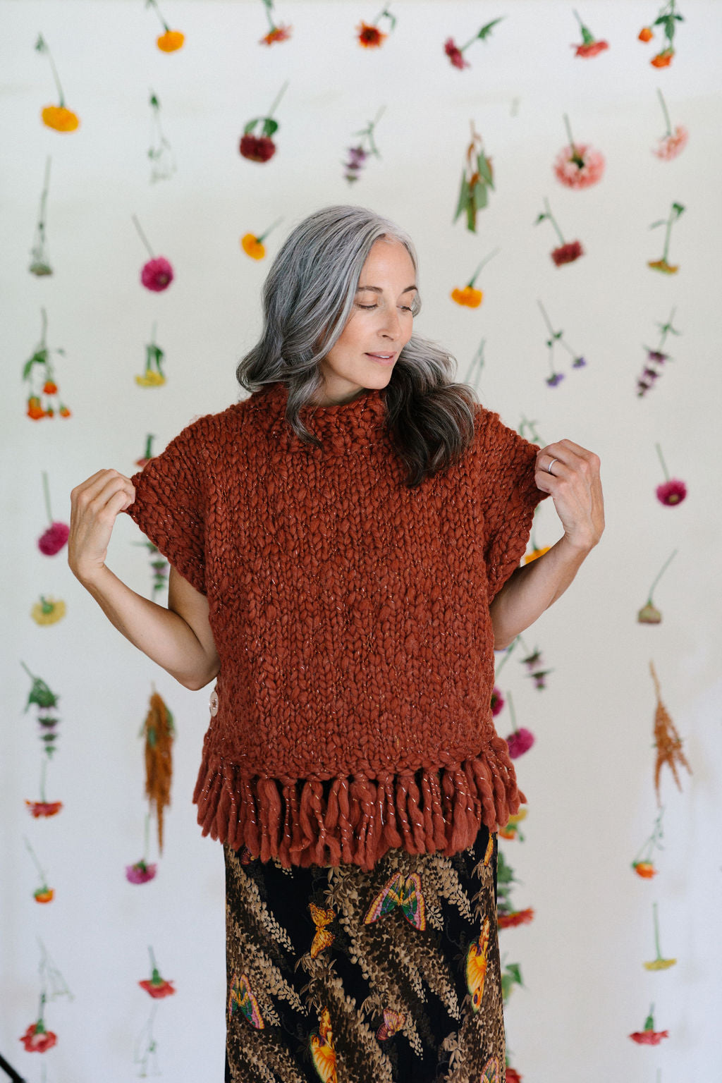 Model standing in front of a flower backdrop showing the sleeves of the Provence Poncho