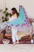 Model holding shawl out behind her to display triangle shape, flowers, and fringe in motion