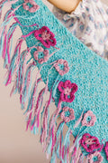 Close up of knit shawl edge displaying yarn fringe and crochet flowers