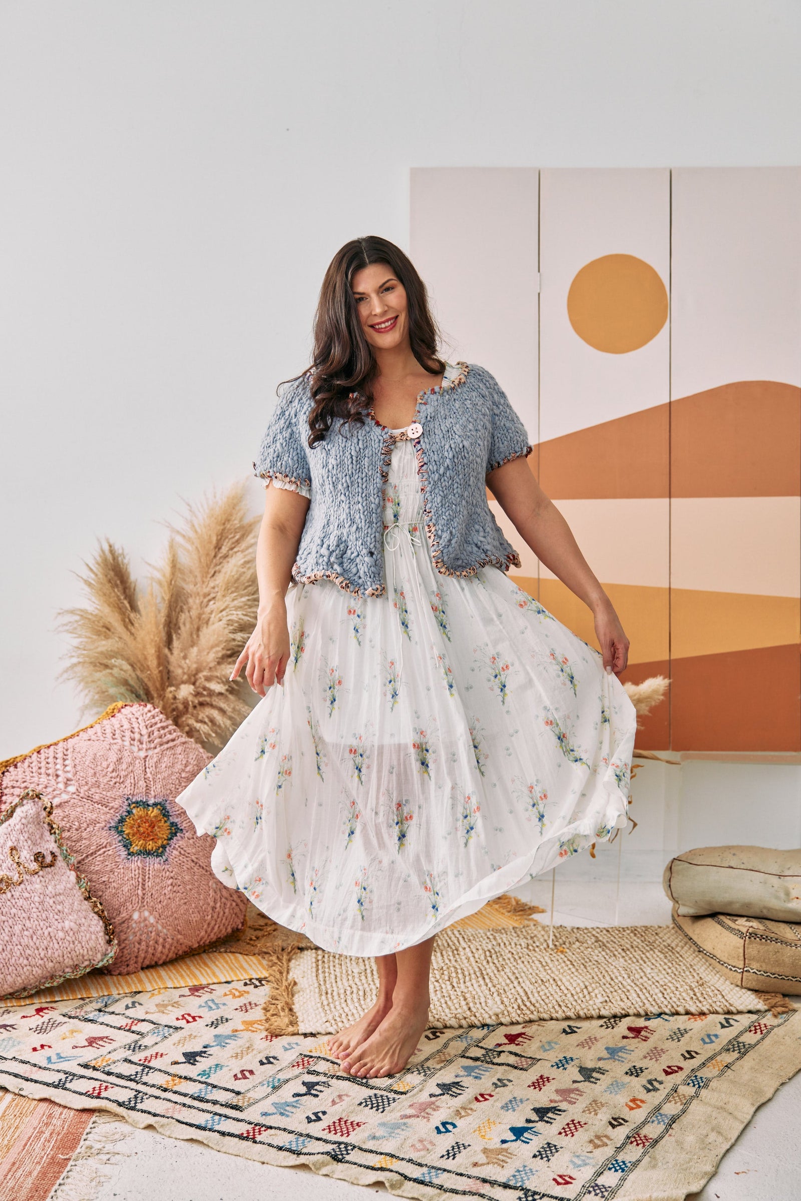 Woman wearing a white dress with flowers and a short sleeve light blue cardigan