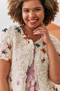 Portrait view of a model wearing a white short sleeve cardigan with colorful embroidery.