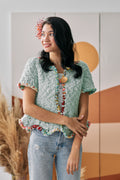 Front view of a short sleeve handknit cardigan with bold bronze circle button closure.
