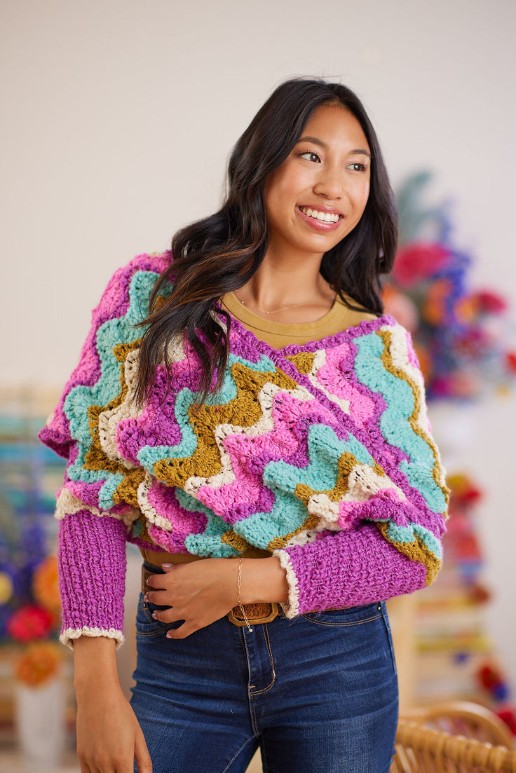Feather and fan lace wrap worn crossed over the front of smiling model, ribbed cuffs on forearms displayed