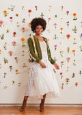 Model standing before a wall of flowers in a white dress with an unbuttoned cardigan