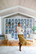 Woman standing in front of a bookshelf models a cream colored cardigan over a gold dress