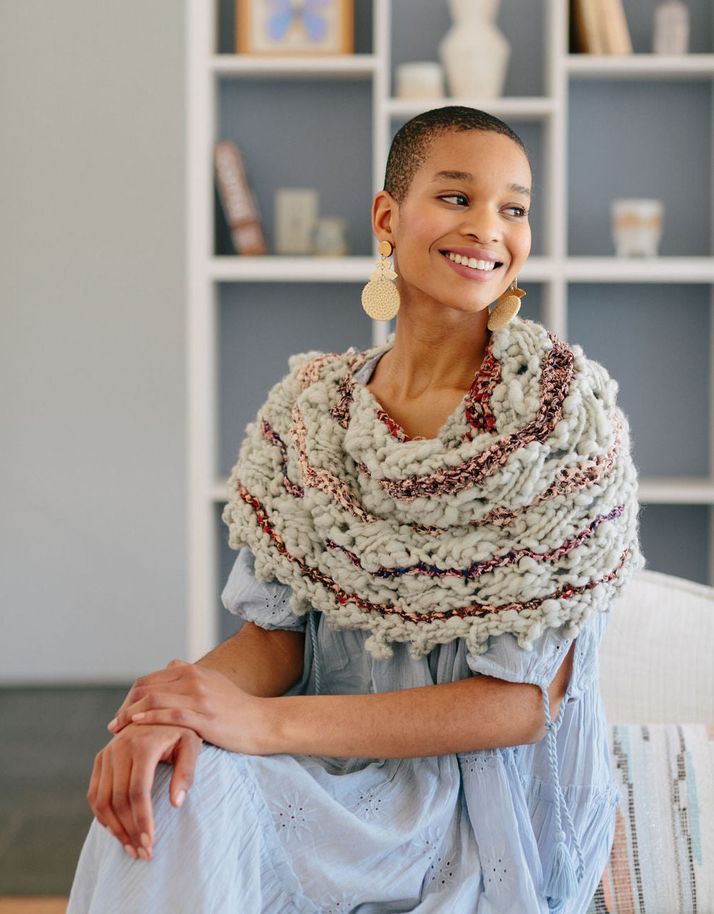 Model smiling with hands on knee wearing a shawl.