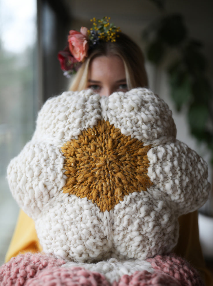 Model holding flower pillow in front of her.